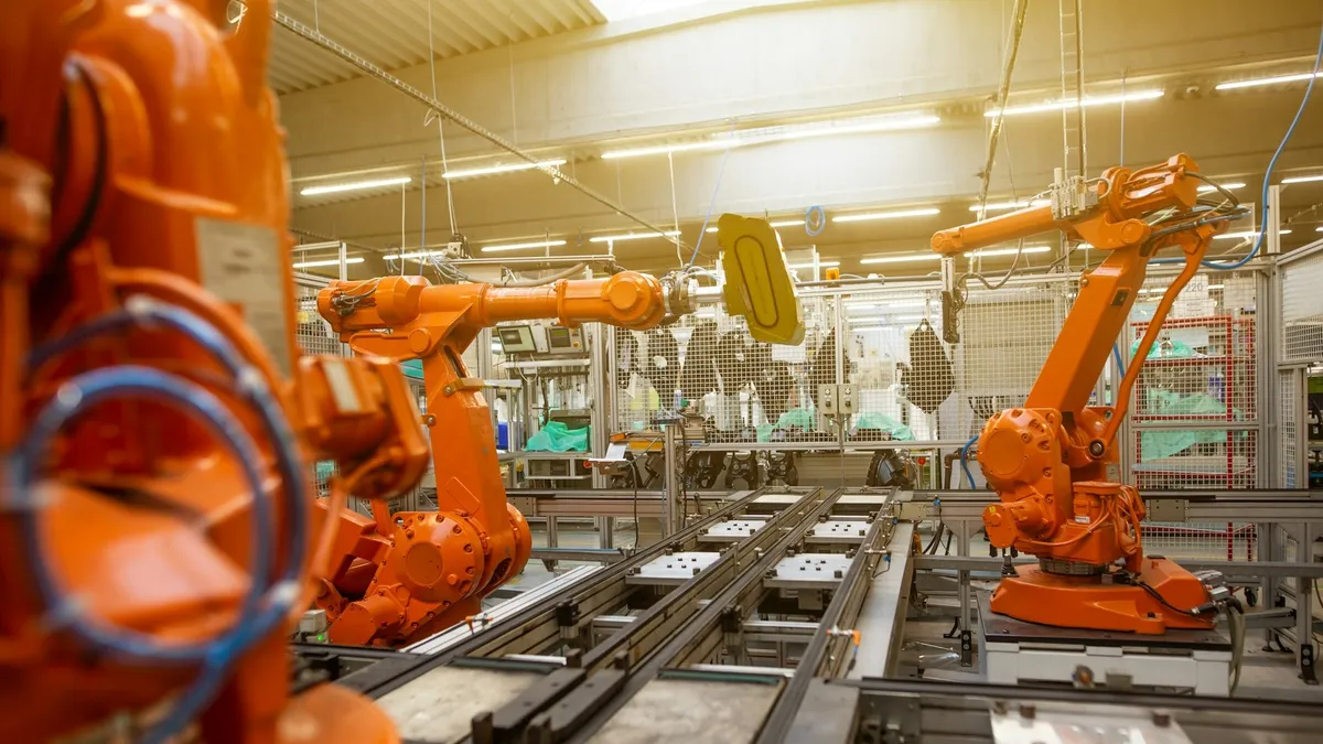 Modern bir fabrikada üretim hattı boyunca dizilmiş turuncu endüstriyel robot kolları